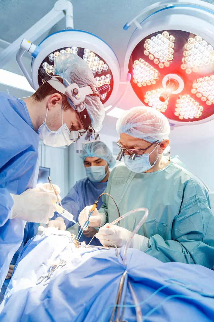 Surgeons in caps, masks and loupes operating under surgical lights