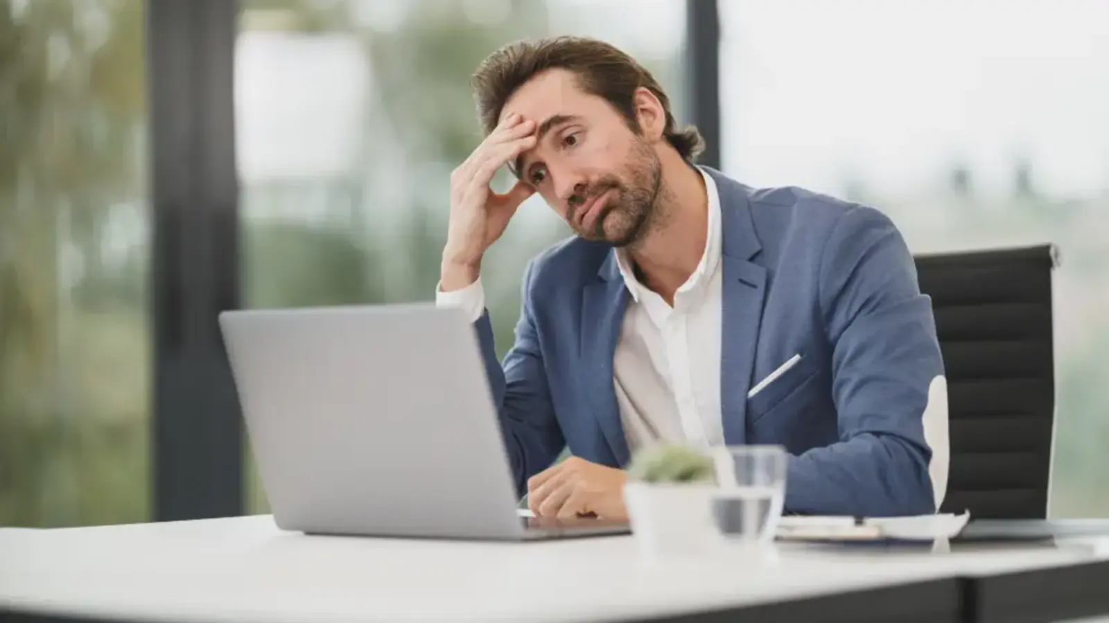 A man at a desk with a laptop, resting his head in his hand