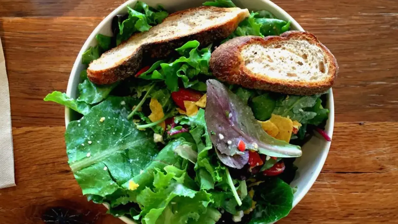 A bowl of green salad with toasted bread, seen from above