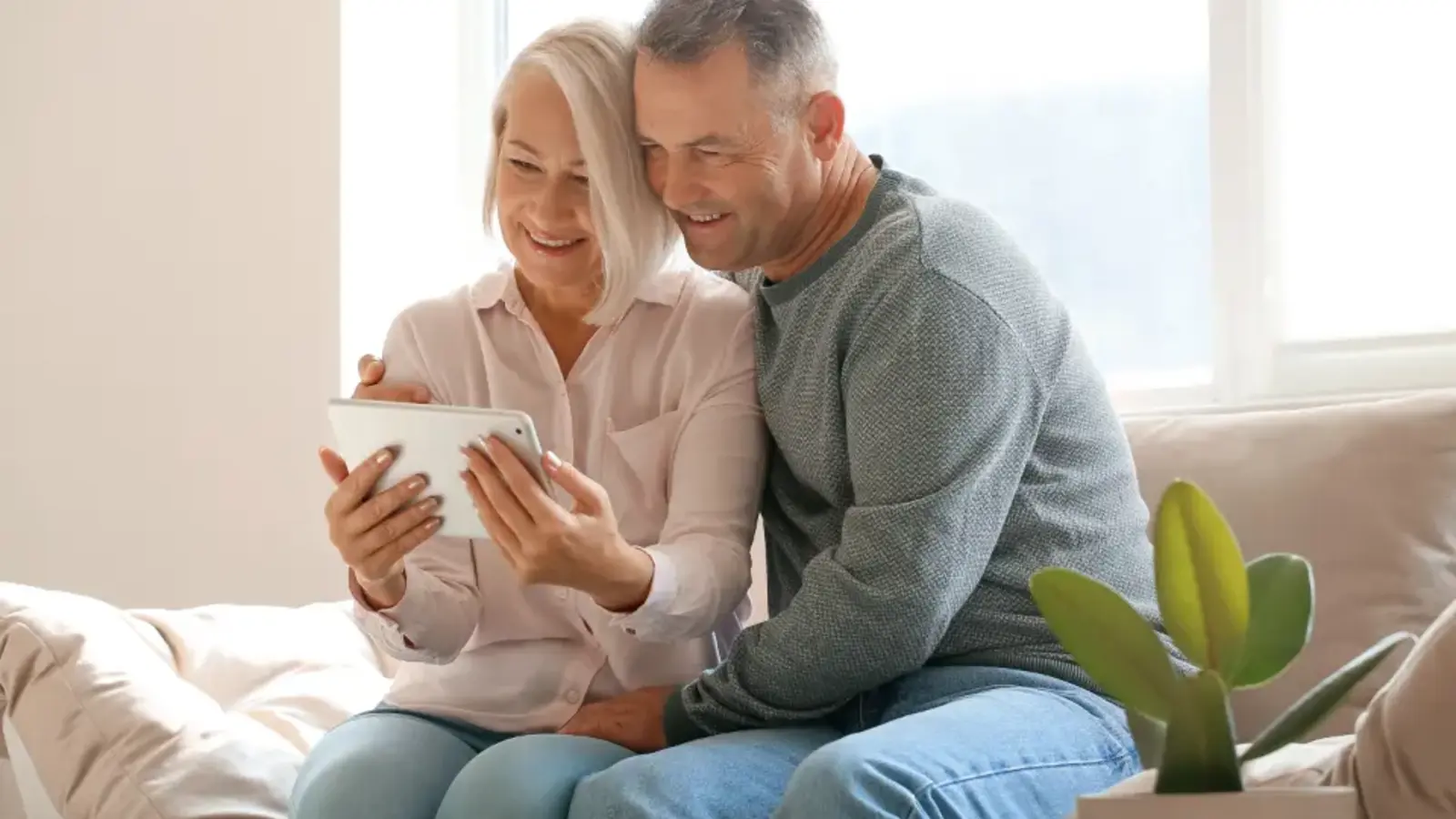 A middle-aged couple sitting together on a sofa looking at a tablet