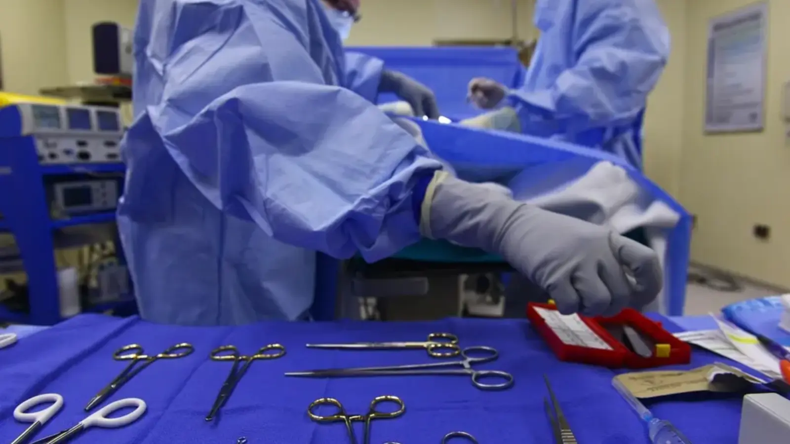 Surgical instruments laid out on a blue drape with surgeons working in the background