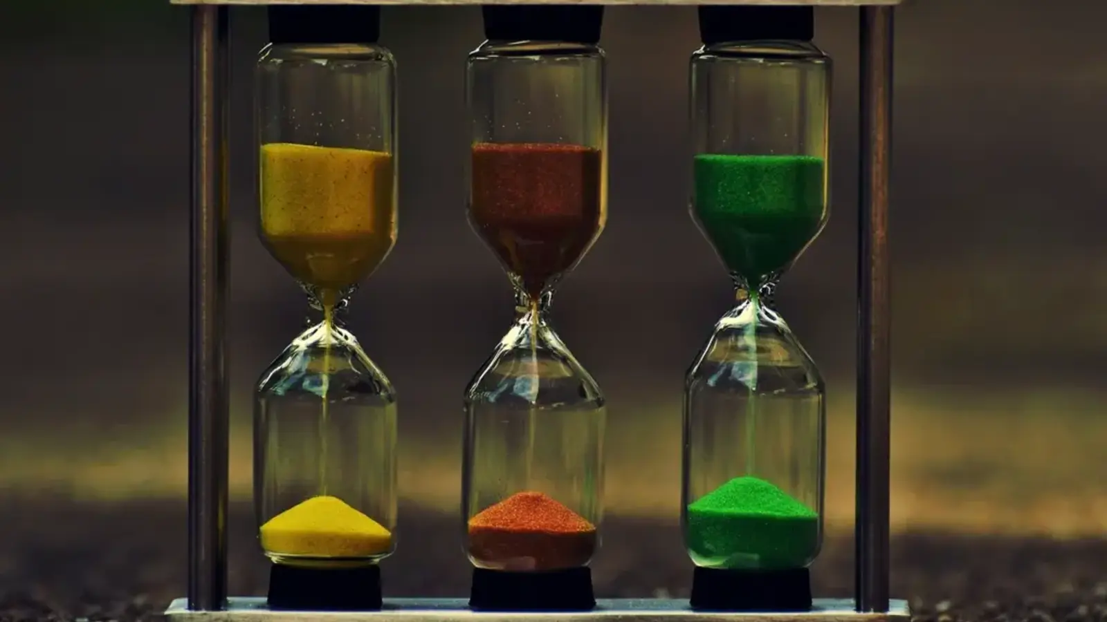Three hourglasses with yellow, orange and green sand standing in a wooden frame