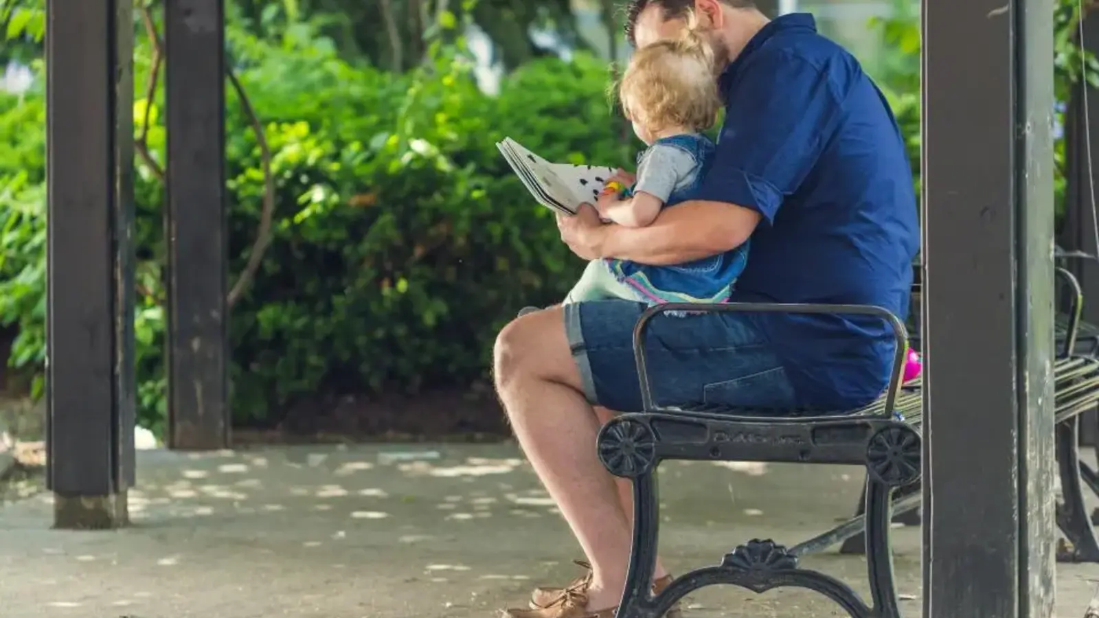 A father sitting on a park bench reading with his young child