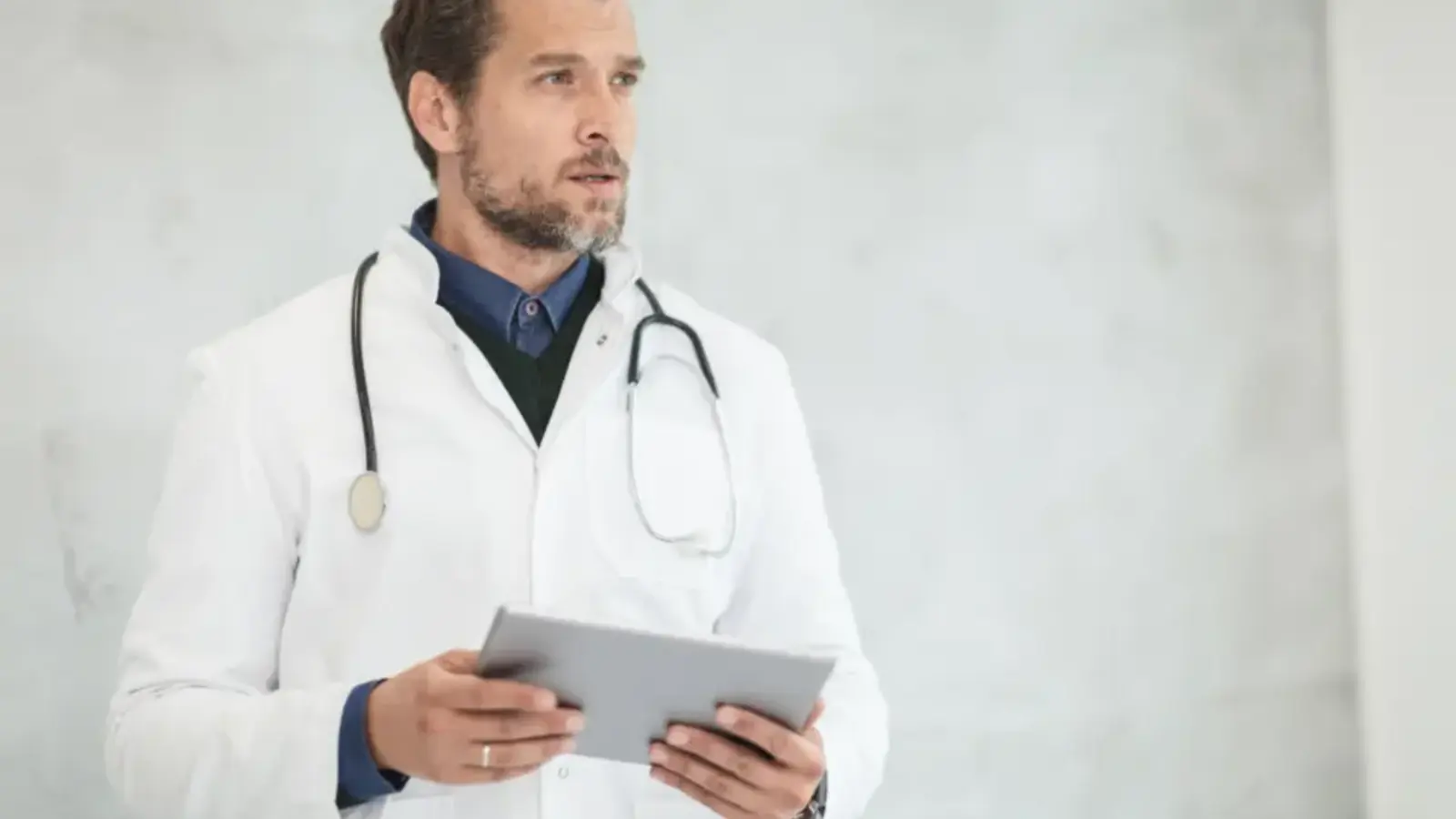 A doctor in a white coat with a stethoscope holding a tablet