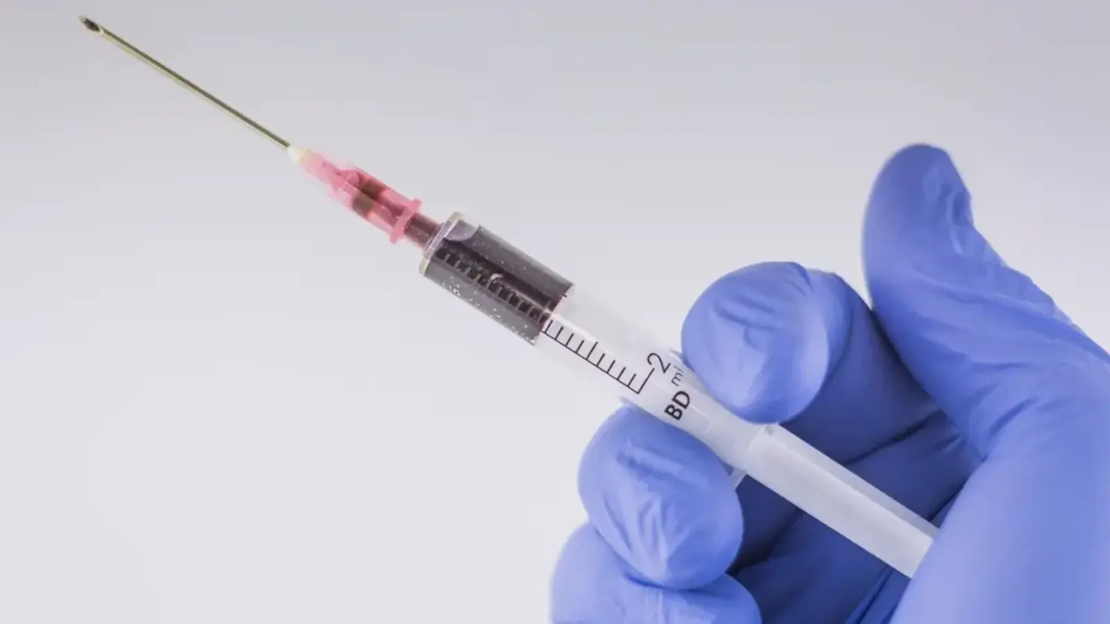 A gloved hand holding a small syringe against a pale background