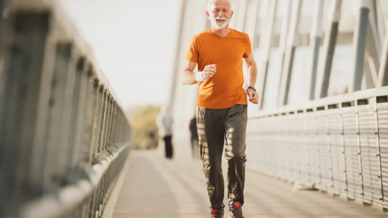 An older man in an orange shirt running across a bridge