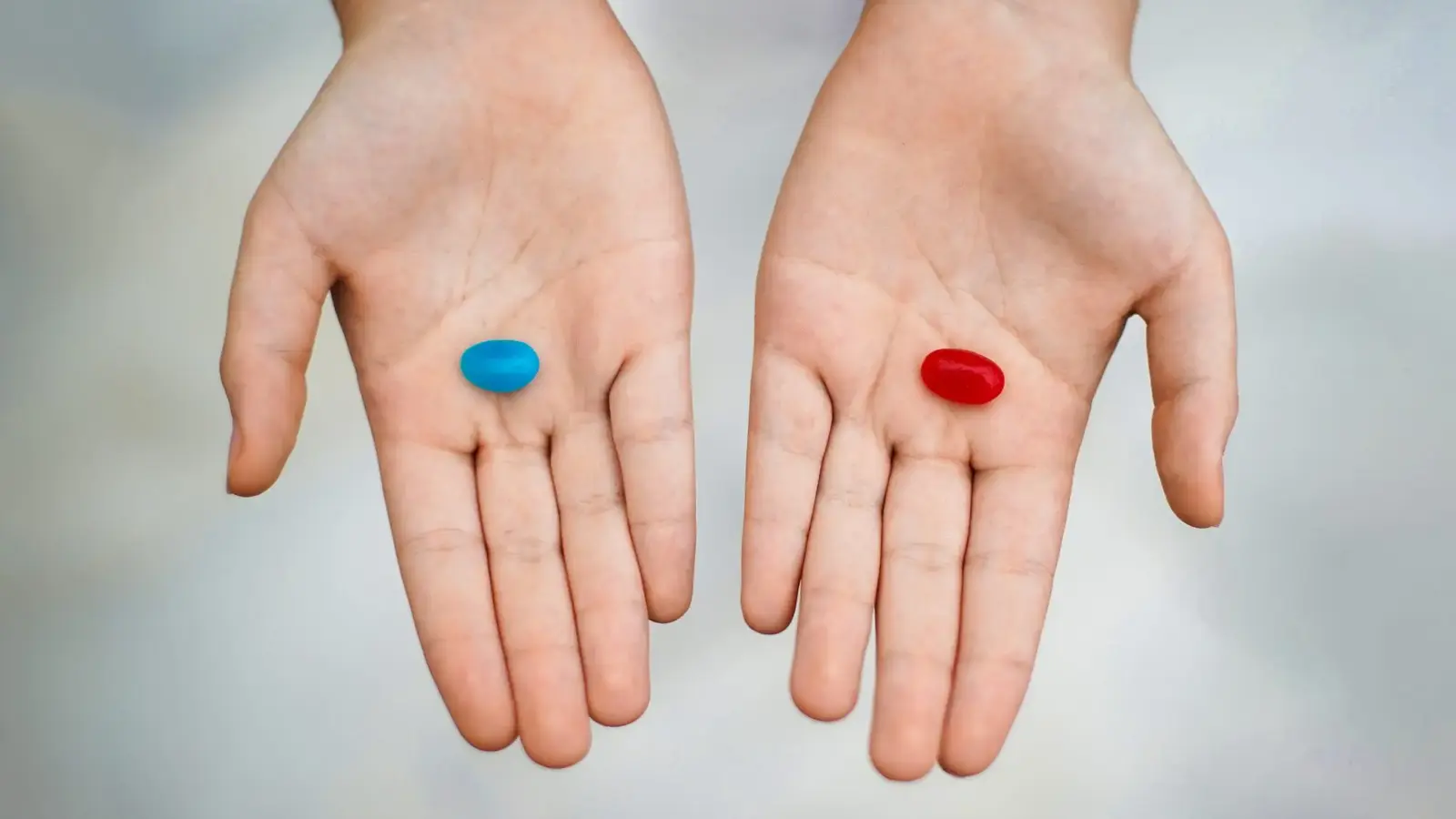 Two open hands, one holding a blue pill and the other a red pill