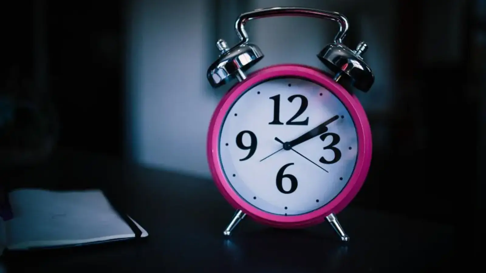 A pink alarm clock on a dark bedside table