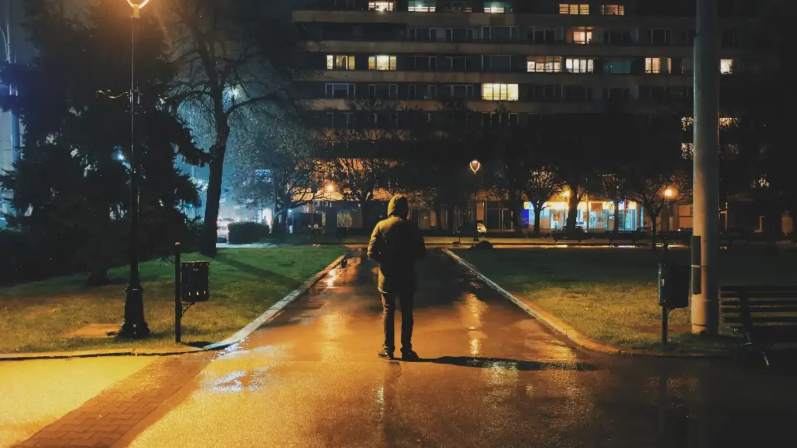 A man walking along a street lit by lamps at night