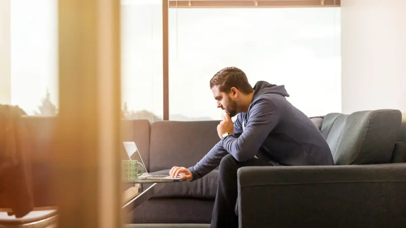 A man sitting on a sofa with a laptop, looking tired