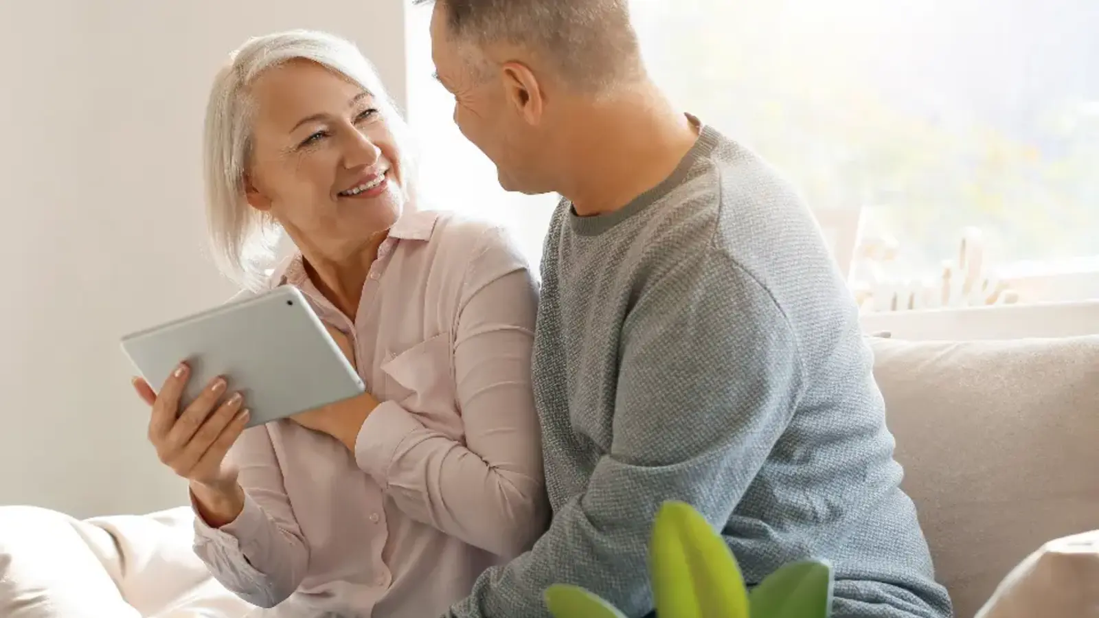 A middle-aged couple talking on a sofa, one holding a tablet