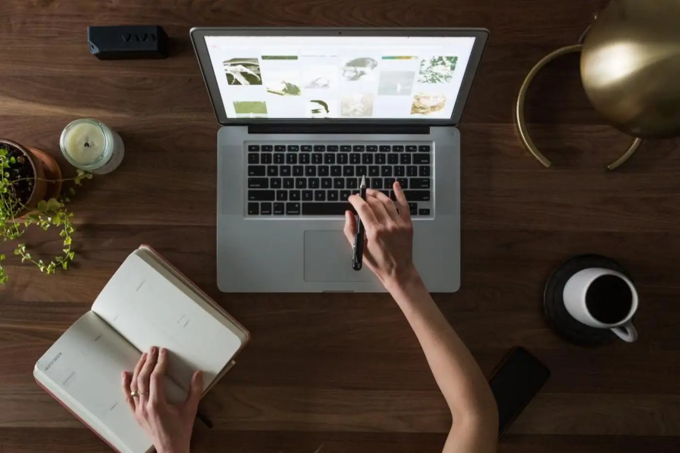 Overhead view of hands writing in a notebook beside a laptop