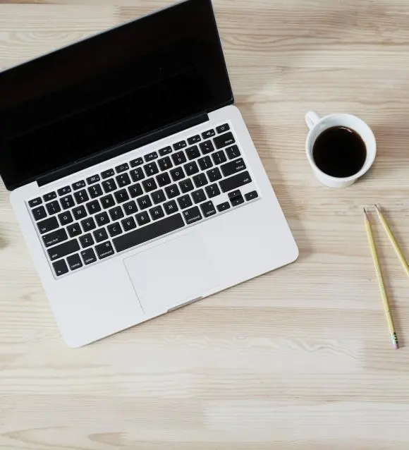 Open laptop on a light wooden desk with a coffee cup